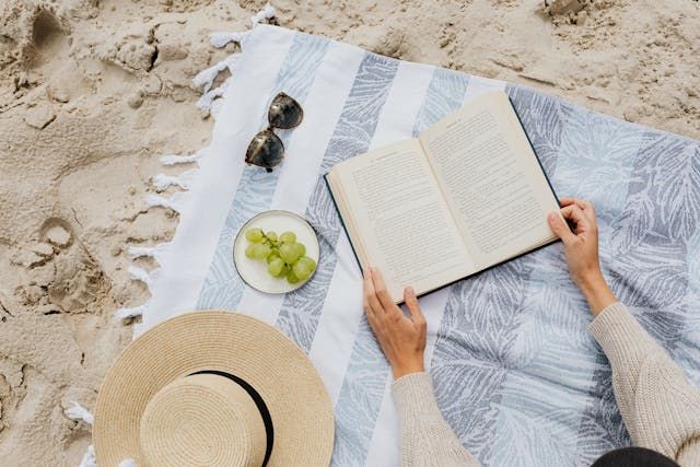 Lady on the beach sitting on a towel reading a book