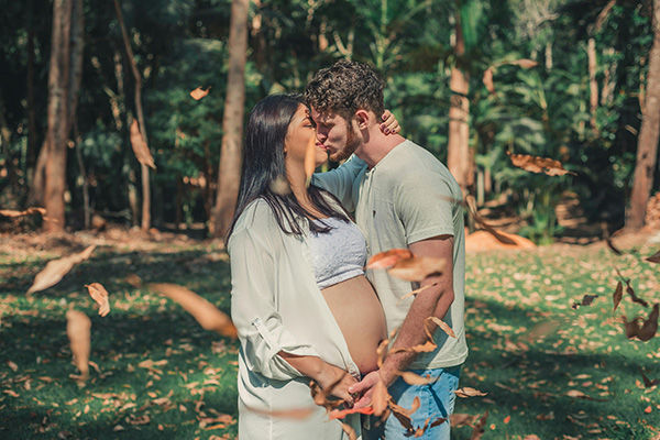 pregnant woman and man kissing in a field on a sunny day