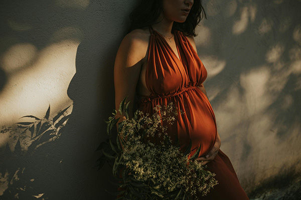 pregnant women in rust coloured dress holding a bouquet of small white flowers 