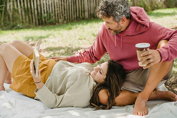 man and pregnant woman laying on blanket reading book on a sunny day