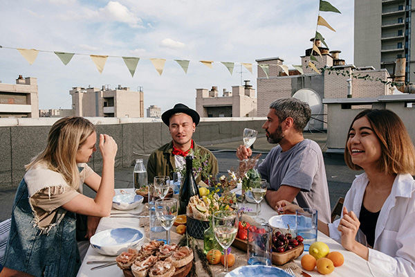 a group of men and women sitting at a table on a rooftop celebrating with dinner and drinks