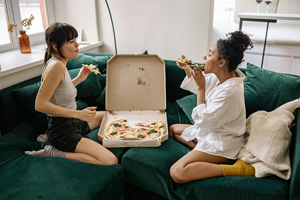 Sexual compatibility female couple on couch happily eating pizza